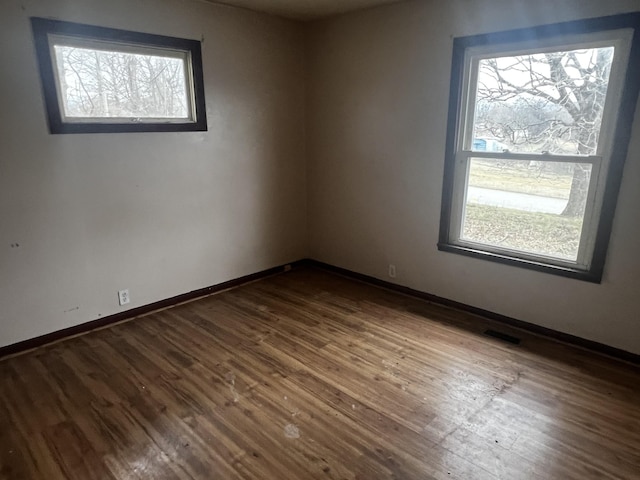 empty room with dark wood-type flooring, baseboards, and visible vents