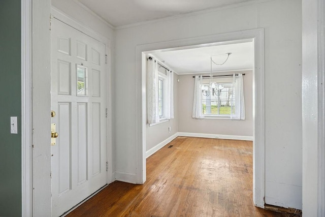 foyer featuring baseboards, an inviting chandelier, crown molding, and wood finished floors