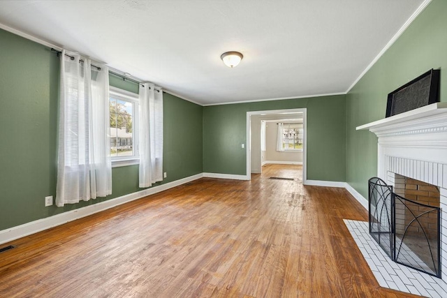 unfurnished living room with crown molding, a fireplace, visible vents, wood finished floors, and baseboards
