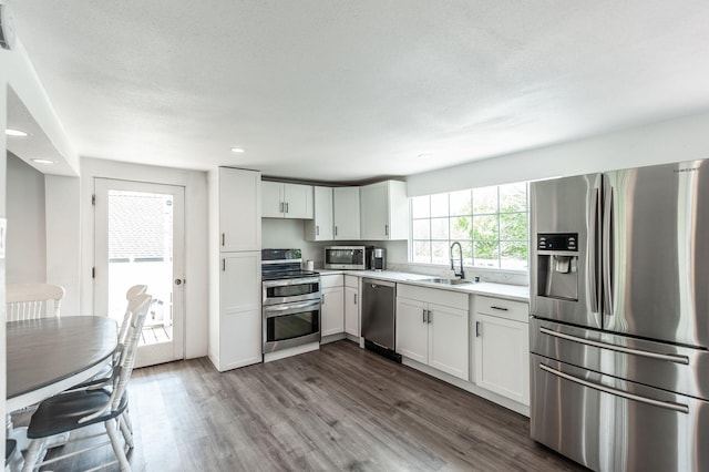 kitchen with white cabinets, appliances with stainless steel finishes, dark wood-style flooring, light countertops, and a sink