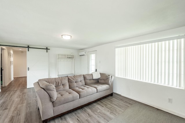 living area featuring wood finished floors, a wall unit AC, baseboards, and a barn door