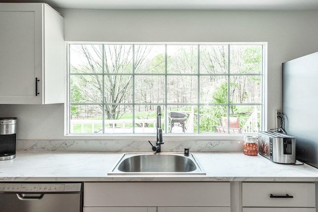 kitchen with stainless steel dishwasher, white cabinets, a sink, and light stone counters