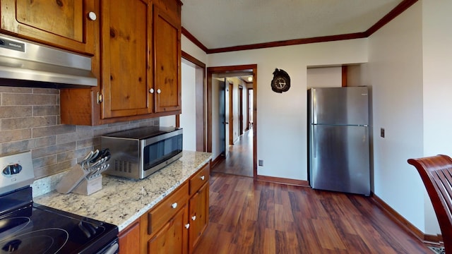 2519 Old Greenbrier Pike, Greenbrier, TN 37073 - kitchen featuring dark wood-style flooring, ornamental molding, under cabinet range hood, brown cabinetry, and appliances with stainless steel finishes