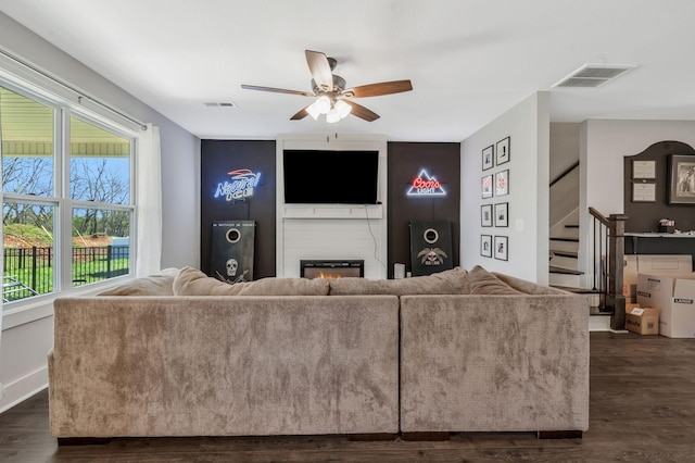 living room featuring dark wood-style floors, a ceiling fan, visible vents, and stairs