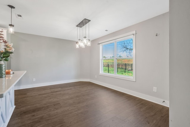 unfurnished dining area featuring a notable chandelier, dark wood-style floors, baseboards, and visible vents