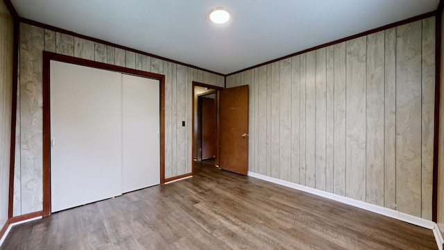 unfurnished bedroom featuring ornamental molding, baseboards, a closet, and wood finished floors