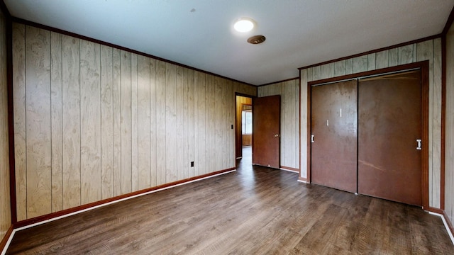 unfurnished bedroom featuring a closet, baseboards, ornamental molding, wood finished floors, and wood walls