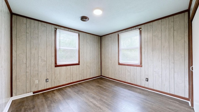 empty room featuring a wealth of natural light, wooden walls, baseboards, and wood finished floors