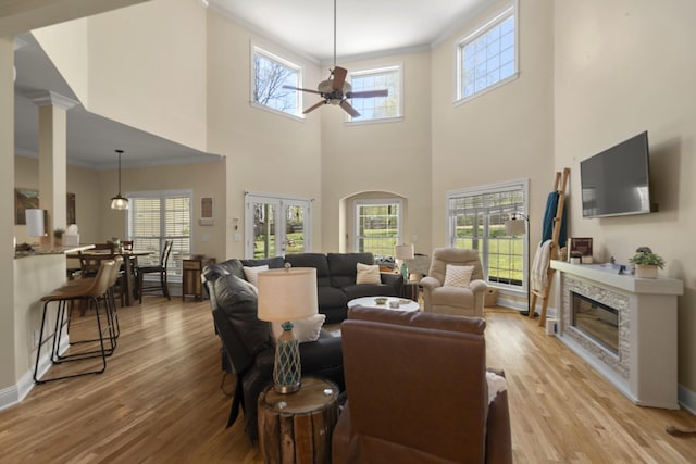 living area featuring baseboards, ornamental molding, light wood-type flooring, a ceiling fan, and a glass covered fireplace