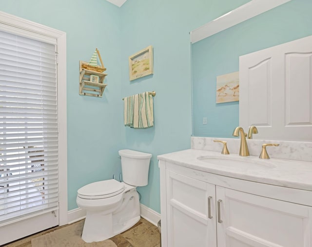 half bath with baseboards, vanity, and toilet