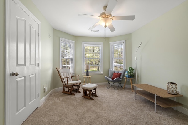 living area with visible vents, baseboards, ceiling fan, and light colored carpet