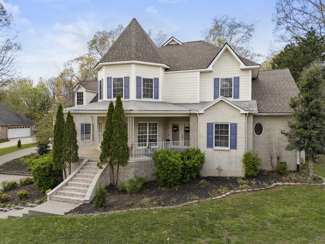 victorian-style house with a shingled roof, covered porch, a front yard, brick siding, and stairs