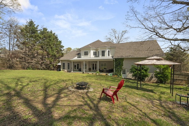 back of property with a shingled roof, fence, a fire pit, and a lawn
