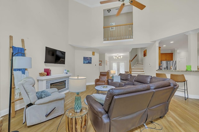 living room with light wood-type flooring, a ceiling fan, baseboards, and stairway