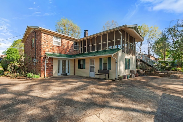 back of house with a chimney, driveway, stairs, brick siding, and a sunroom