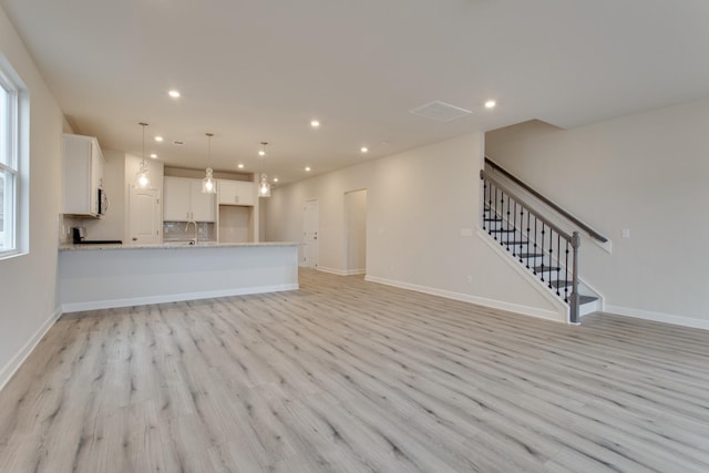 unfurnished living room featuring baseboards, a sink, stairway, light wood finished floors, and recessed lighting