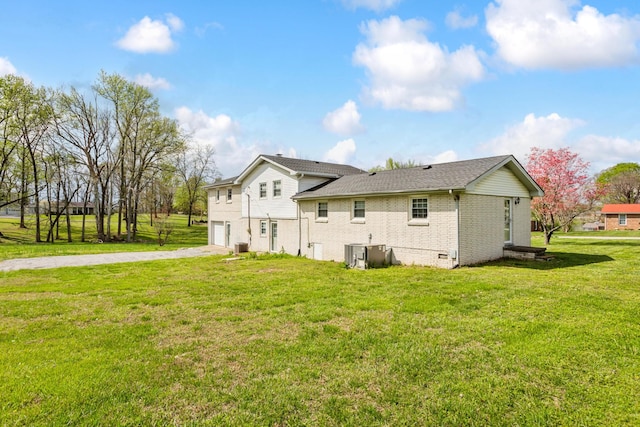 back of house featuring cooling unit, a lawn, brick siding, an attached garage, and driveway
