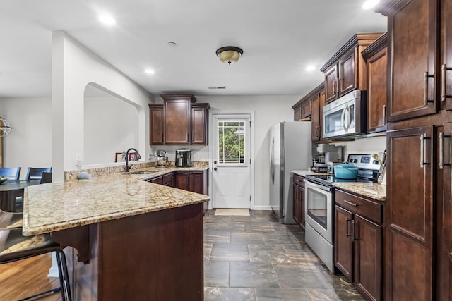 kitchen featuring a sink, appliances with stainless steel finishes, a kitchen breakfast bar, a peninsula, and light stone countertops