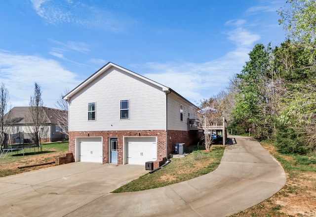 view of side of property featuring a trampoline, concrete driveway, cooling unit, brick siding, and a garage