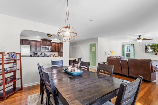 dining space with arched walkways, light wood-style floors, ceiling fan with notable chandelier, and recessed lighting