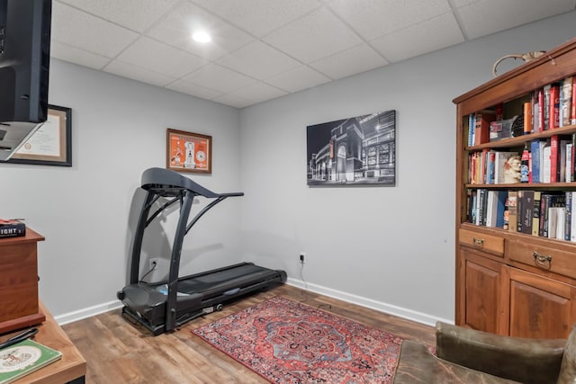 exercise room featuring a paneled ceiling, wood finished floors, and baseboards