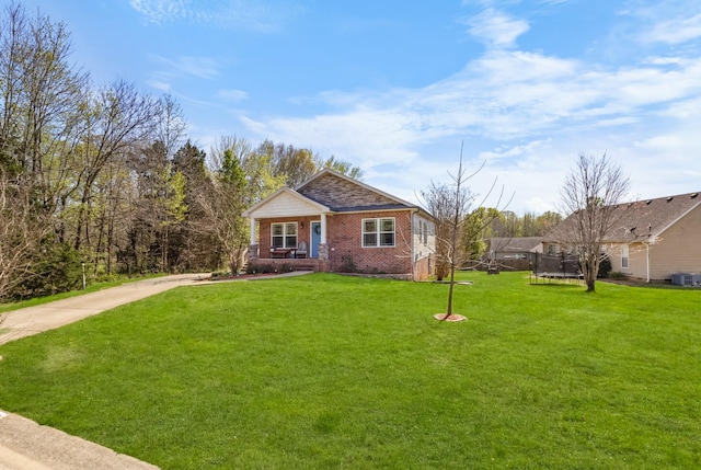 view of front of house with a trampoline, a front yard, brick siding, and driveway