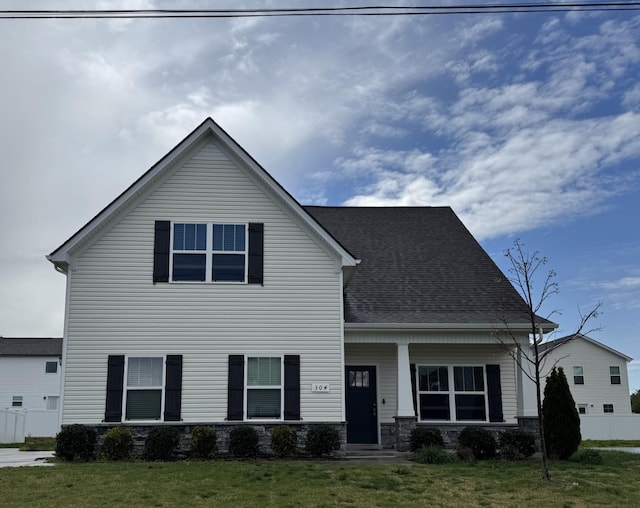 view of front of home featuring a front yard, roof with shingles, stone siding, and fence