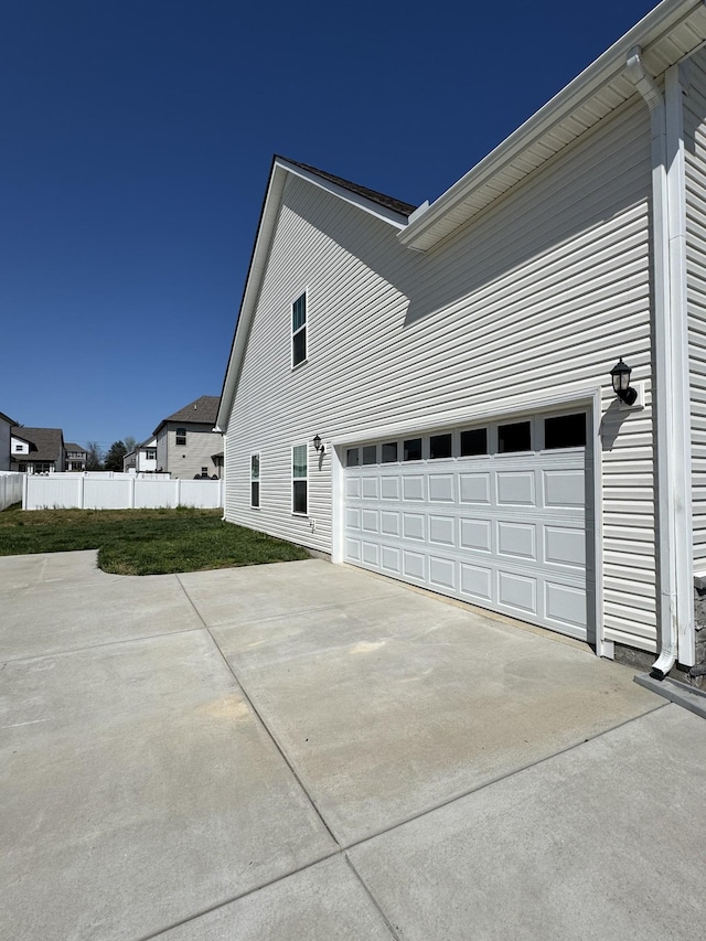view of side of home with an attached garage, driveway, fence, and a lawn