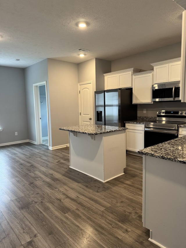 kitchen with a textured ceiling, white cabinetry, a kitchen island, dark stone counters, and stainless steel appliances