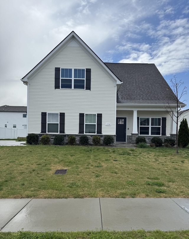 traditional-style home featuring roof with shingles and a front lawn