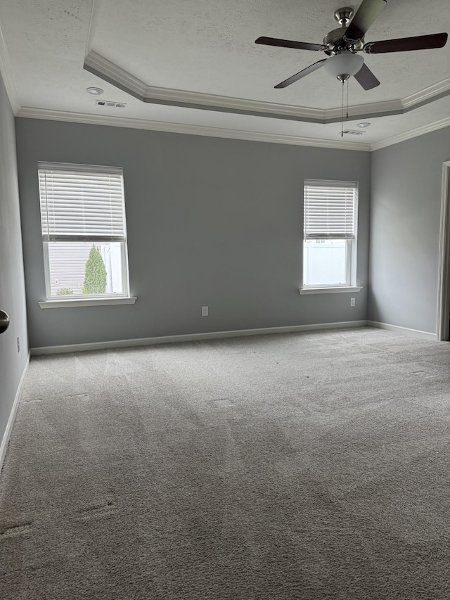 carpeted empty room with visible vents, baseboards, a raised ceiling, ornamental molding, and a ceiling fan