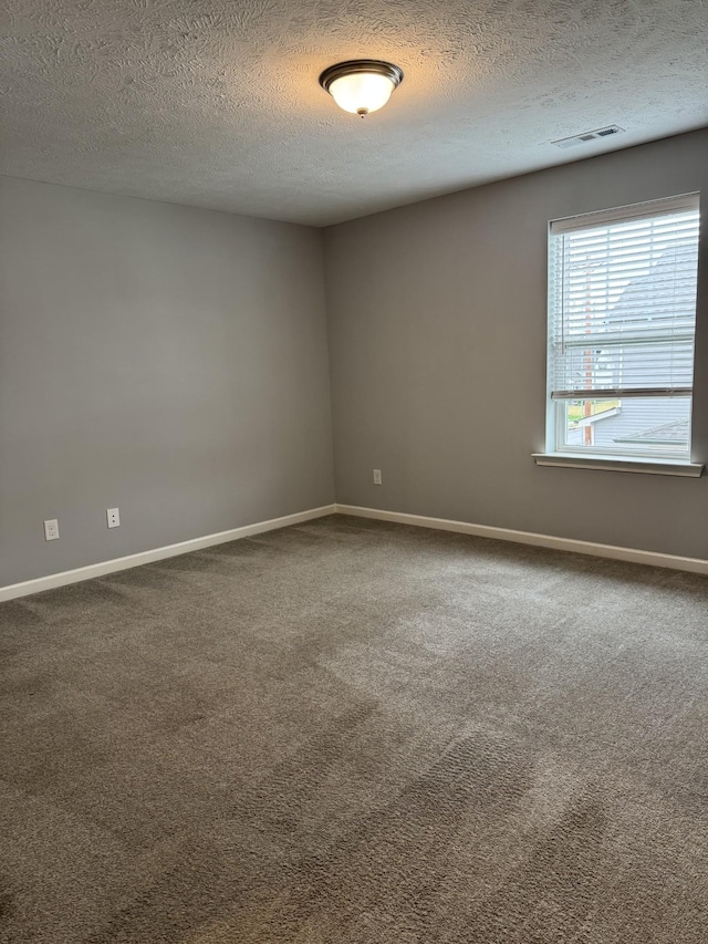 empty room featuring dark colored carpet, visible vents, baseboards, and a textured ceiling