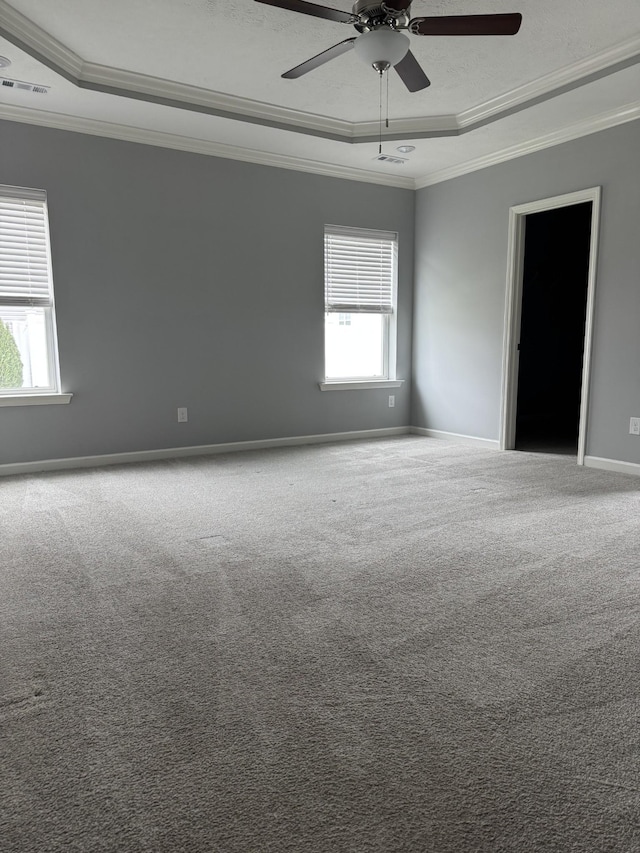 carpeted spare room with crown molding, visible vents, a wealth of natural light, and a raised ceiling