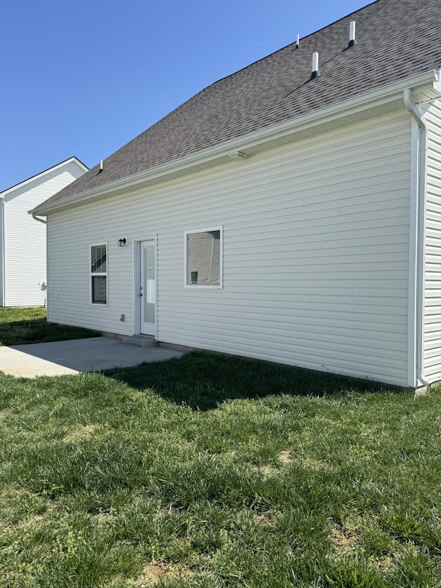 rear view of property with a yard, a patio, and roof with shingles
