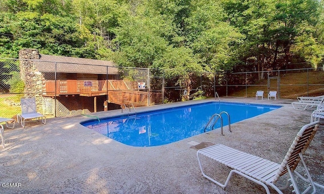 community pool featuring a patio, a forest view, and fence