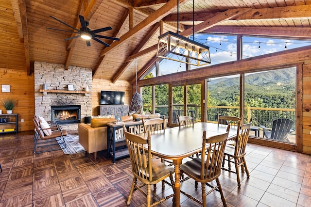 dining area featuring a ceiling fan, a fireplace, wood ceiling, beam ceiling, and wood walls