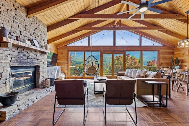 living room with a stone fireplace, wood walls, beamed ceiling, ceiling fan, and wood ceiling