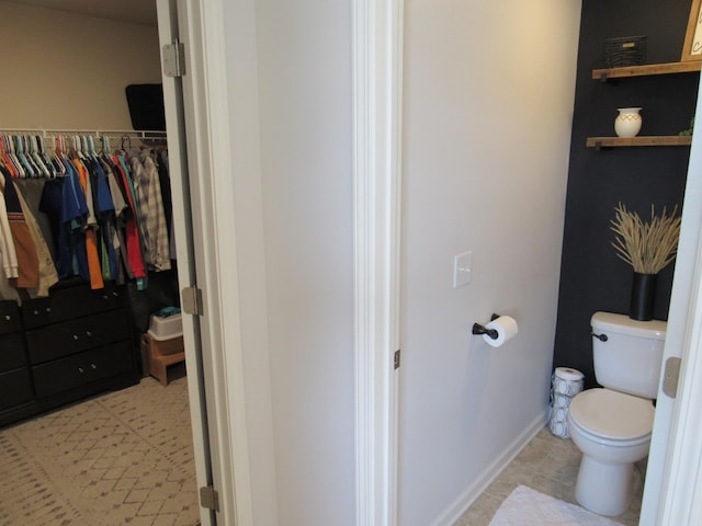 bathroom with toilet, a walk in closet, tile patterned flooring, and baseboards