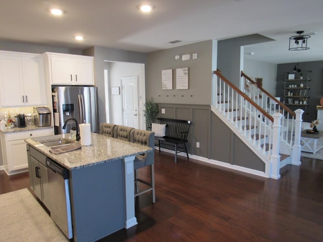 kitchen featuring white cabinets, appliances with stainless steel finishes, light stone counters, a sink, and dark wood-style floors