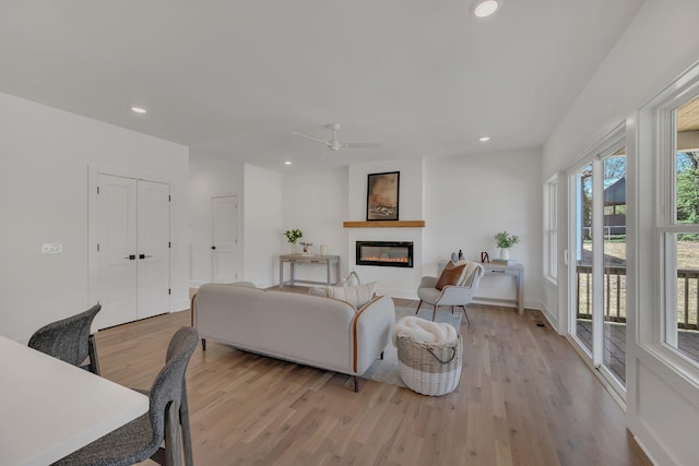 living area with light wood-type flooring, ceiling fan, a glass covered fireplace, and recessed lighting