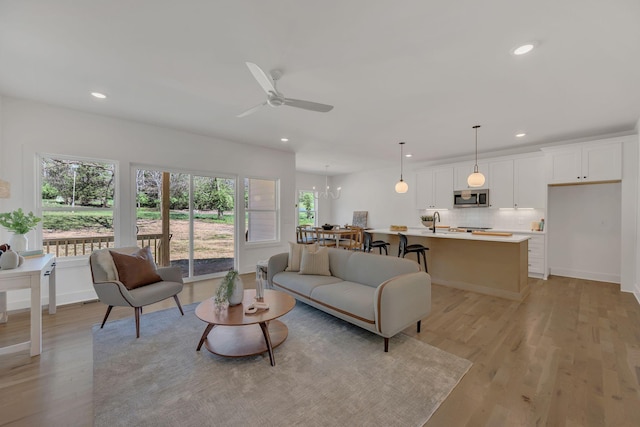 living area featuring recessed lighting, light wood finished floors, and ceiling fan with notable chandelier