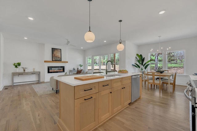 kitchen featuring a sink, light countertops, appliances with stainless steel finishes, light wood-style floors, and a glass covered fireplace