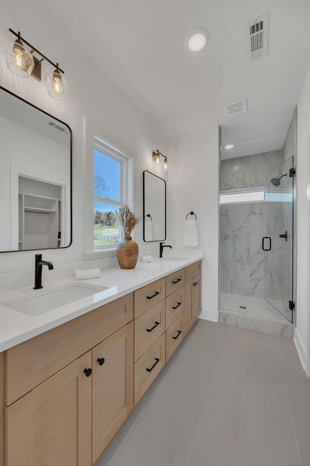 full bath featuring double vanity, visible vents, a sink, and a marble finish shower