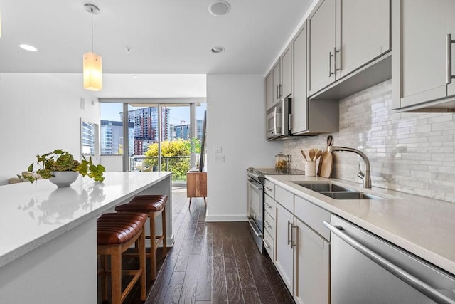 kitchen featuring dark wood-style flooring, light countertops, a sink, stainless steel appliances, and a breakfast bar area