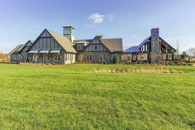 back of property with a standing seam roof, a chimney, metal roof, a lawn, and stone siding