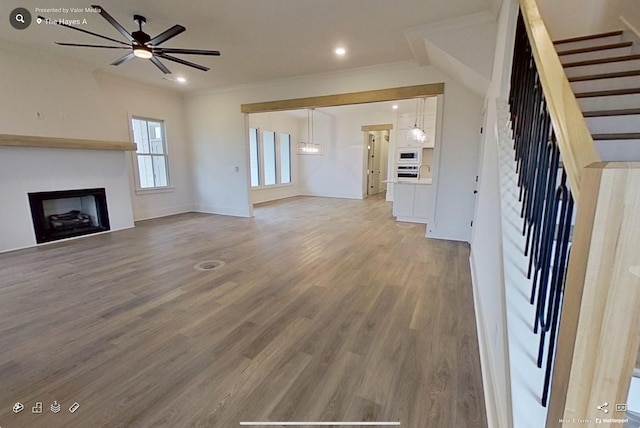 unfurnished living room with crown molding, light wood-style floors, a fireplace, and a ceiling fan