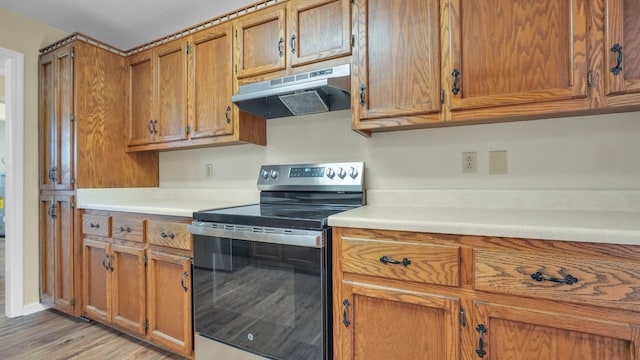 kitchen with under cabinet range hood, light countertops, electric stove, brown cabinets, and light wood finished floors