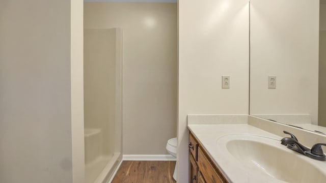bathroom featuring vanity, toilet, wood finished floors, walk in shower, and baseboards