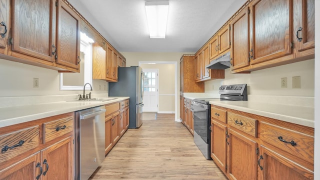 kitchen featuring light wood-style floors, appliances with stainless steel finishes, under cabinet range hood, a sink, and brown cabinets
