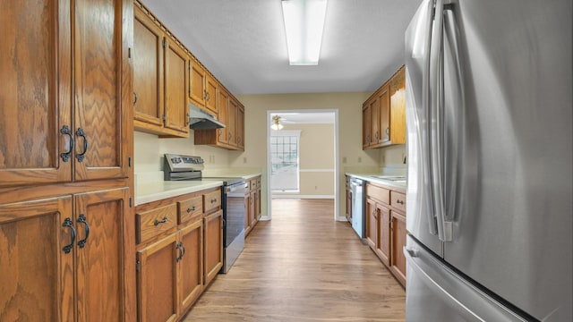 kitchen with light wood-style floors, brown cabinetry, under cabinet range hood, light countertops, and stainless steel appliances